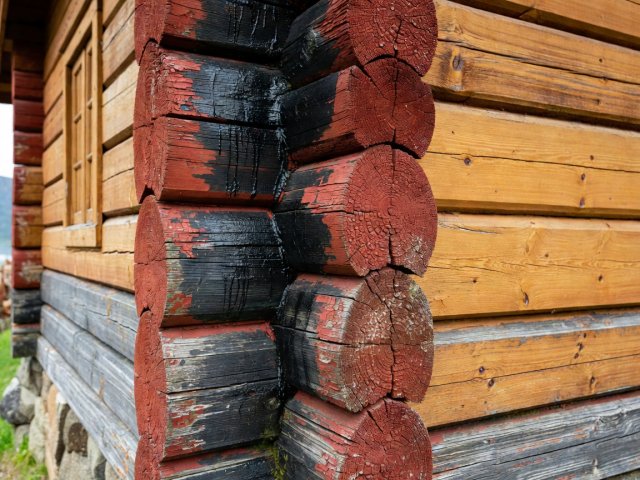 Close-up of weathered red-ochre and pine-tarred log joinery on a historic boathouse in Lærdalsøyri